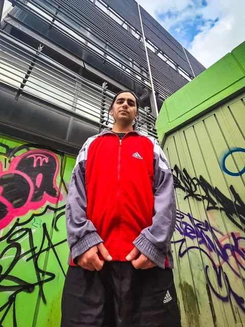 Modelo con campera deportiva roja y gris frente a un graffiti
