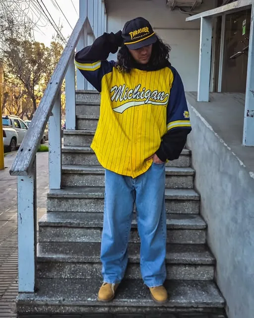 Modelo con jersey de béisbol amarillo y jean ancho en una escalera